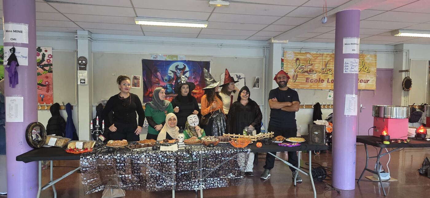 Équipe de bénévoles déguisée en sorcières devant la table de gâteaux du goûter d'Halloween